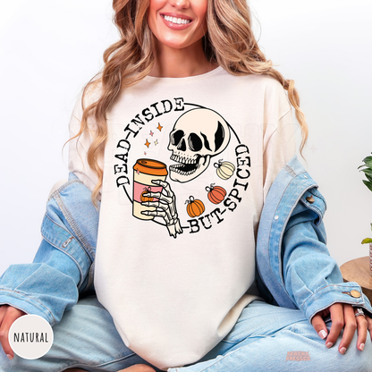 Woman wearing a natural graphic t-shirt with a funny skeleton drinking pumpkin spice coffee and autumn pumpkins.