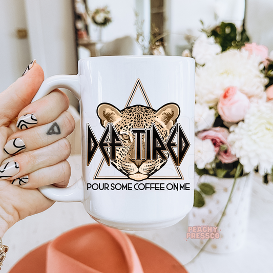 White ceramic coffee mug featuring a leopard face with the funny phrase "Def Tired – Pour Some Coffee On Me" in rock-inspired typography.