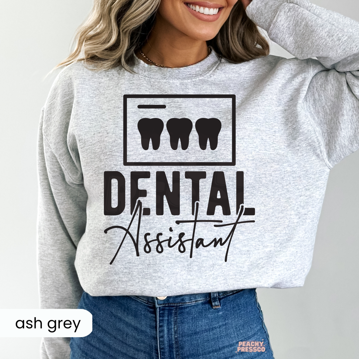 Woman modeling an ash grey Dental Assistant crewneck sweatshirt with black tooth illustration and typography, a dental assistant gift.