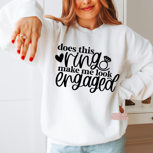 White crewneck sweatshirt featuring the funny "Does This Ring Make Me Look Engaged" graphic with a diamond ring illustration, ideal for engagement announcements, bridal events, bachelorette weekends, and wedding celebrations.