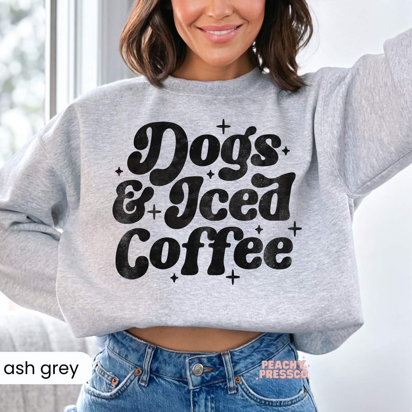 Woman wearing an ash grey cropped sweatshirt with a distressed "Dogs & Iced Coffee" graphic.