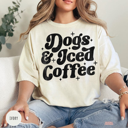 Woman wearing an ivory oversized t-shirt featuring a retro "Dogs & Iced Coffee" graphic with distressed lettering.