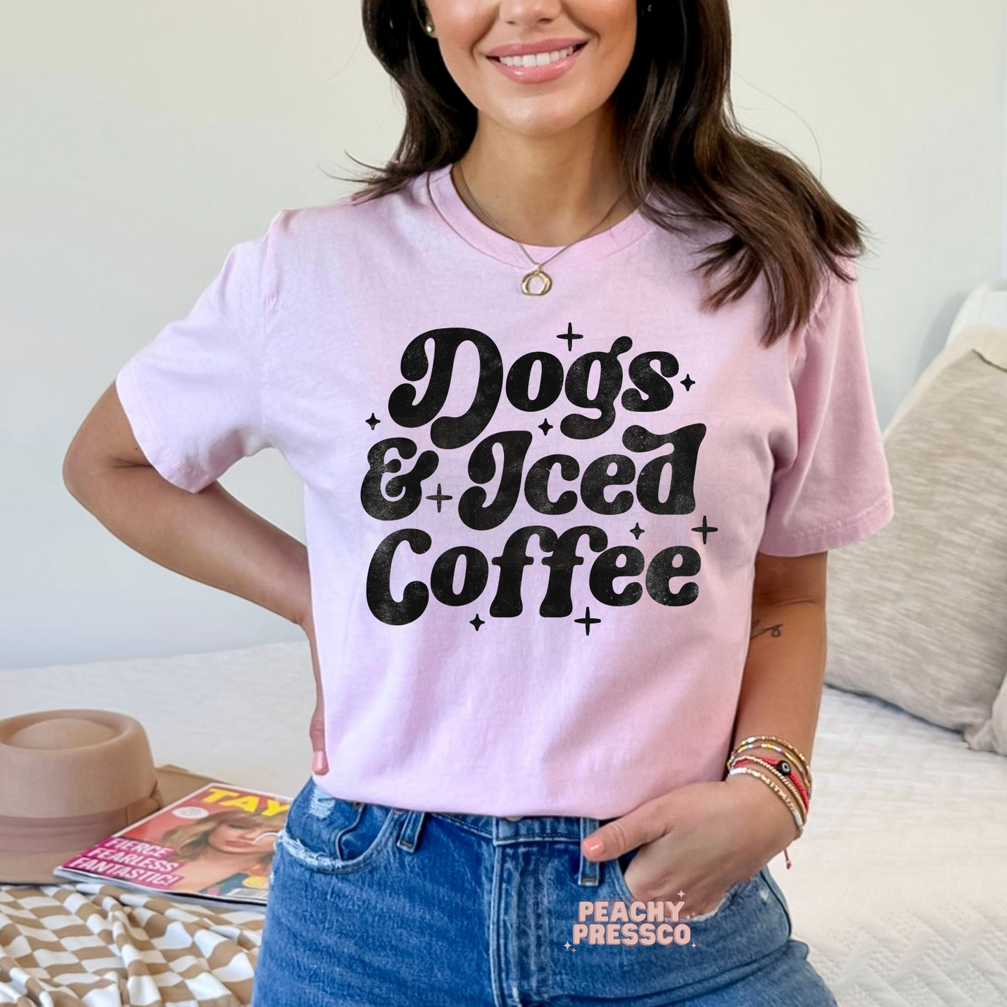 Woman wearing a light pink t-shirt with a vintage "Dogs & Iced Coffee" graphic design in distressed black print.