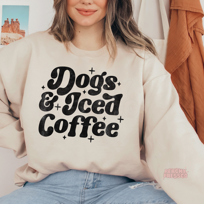 Woman wearing a beige crewneck sweatshirt with a vintage "Dogs & Iced Coffee" graphic in bold retro typography.