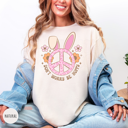 Woman wearing a natural colored Easter graphic t-shirt with a pink leopard bunny ears peace sign and "Don't Worry Be Hoppy" design.