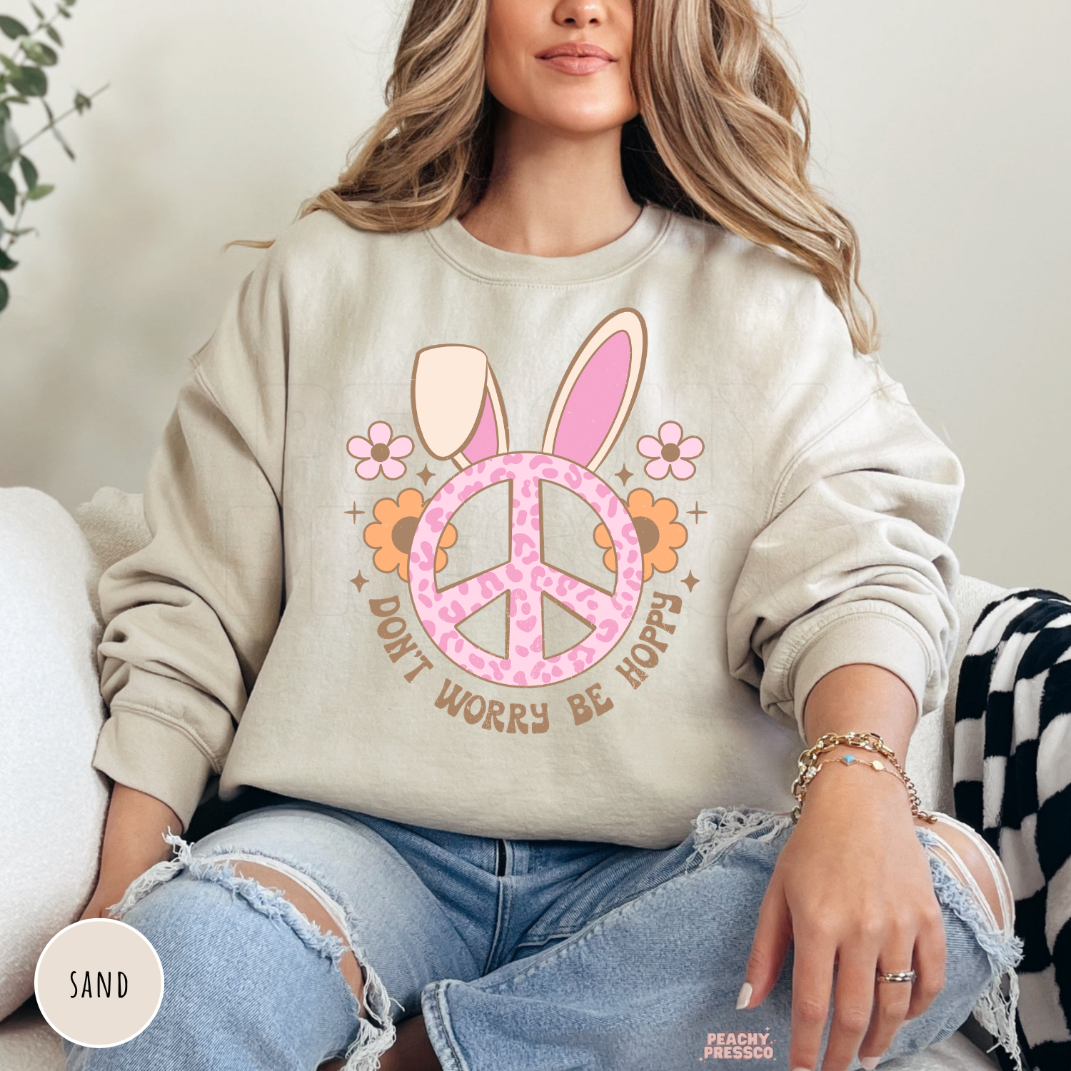 Woman wearing a sand crewneck sweatshirt with a cute Easter bunny ears peace sign graphic and "Don't Worry Be Hoppy" spring design.