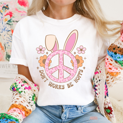Woman wearing a white Easter graphic t-shirt featuring a pink bunny ears peace sign with flowers and the phrase "Don't Worry Be Hoppy."