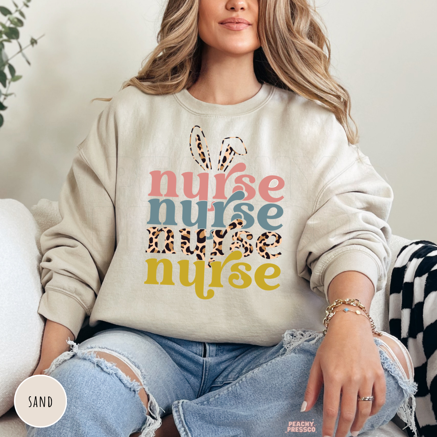 Woman wearing a sand crewneck sweatshirt with a retro Easter Nurse graphic featuring bunny ears, leopard print, and colorful layered typography.