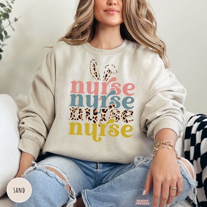 Woman wearing a sand crewneck sweatshirt with a retro Easter Nurse graphic featuring bunny ears, leopard print, and colorful layered typography.