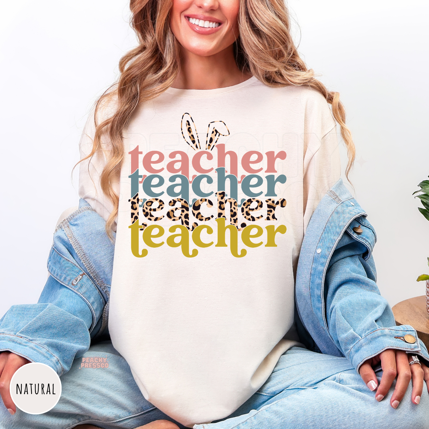 Woman wearing a natural shirt featuring a colorful retro Easter Teacher graphic with bunny ears and leopard print lettering.