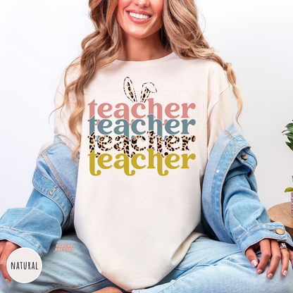 Woman wearing a natural shirt featuring a colorful retro Easter Teacher graphic with bunny ears and leopard print lettering.