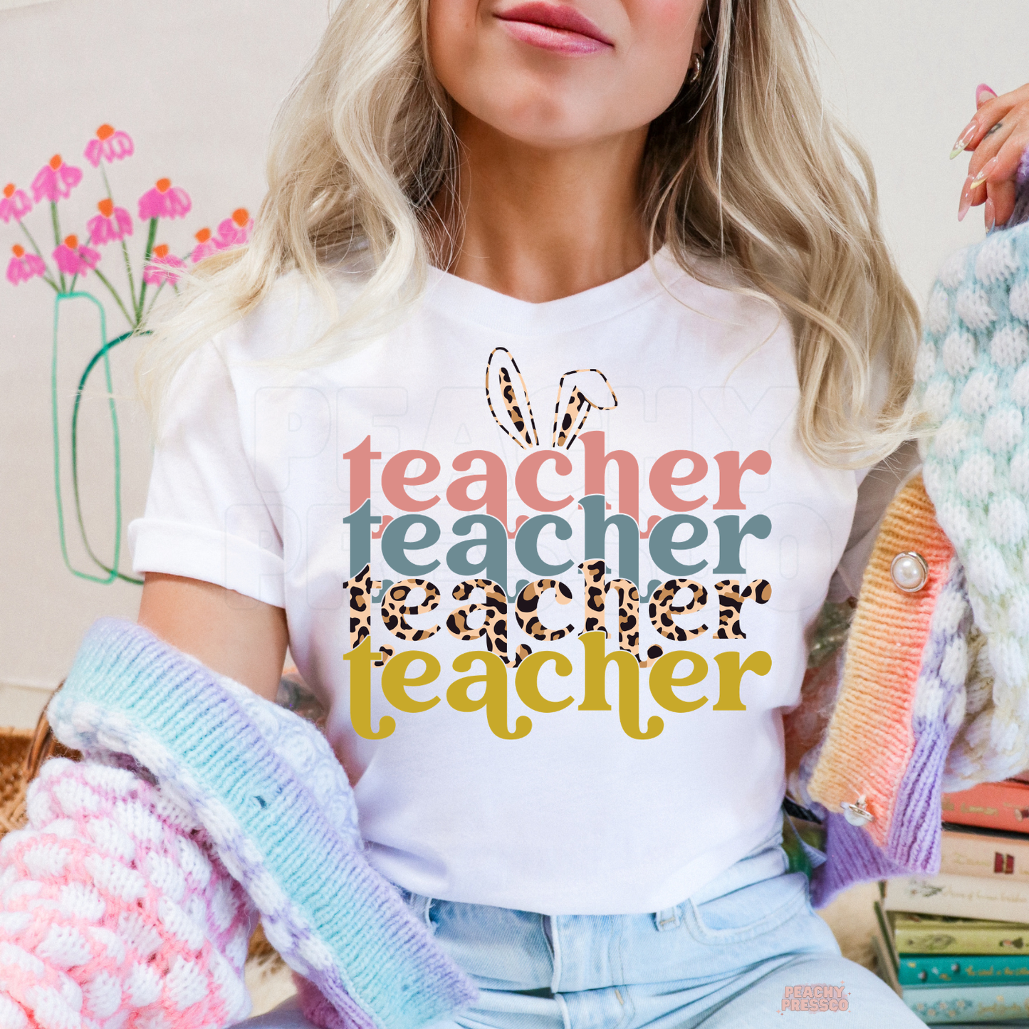 Woman wearing a white t-shirt featuring a retro Easter Teacher design with bunny ears, leopard print lettering, and colorful spring typography.