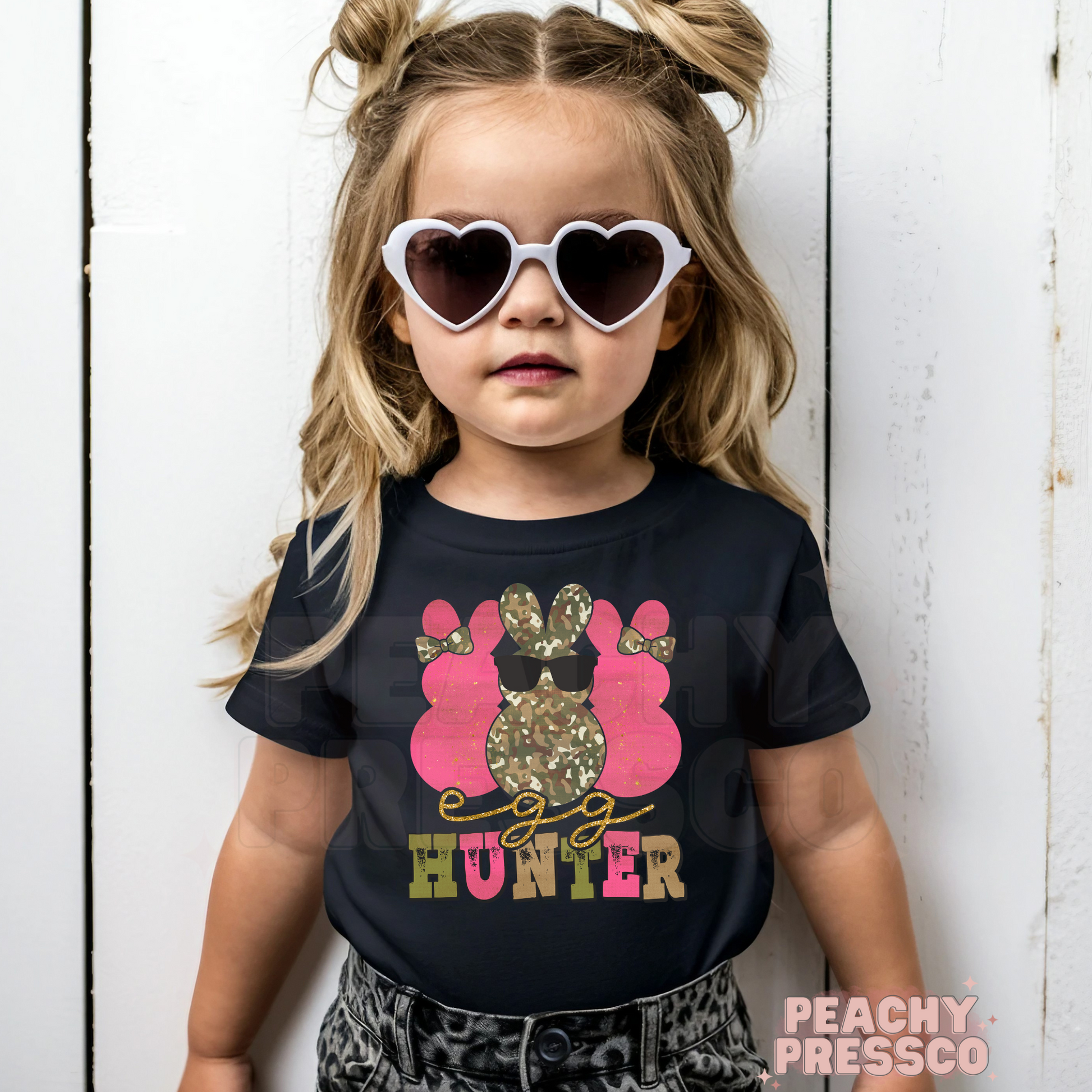 Toddler girl wearing a black Egg Hunter Easter tee with a pink camouflage bunny wearing sunglasses and playful Easter graphic.