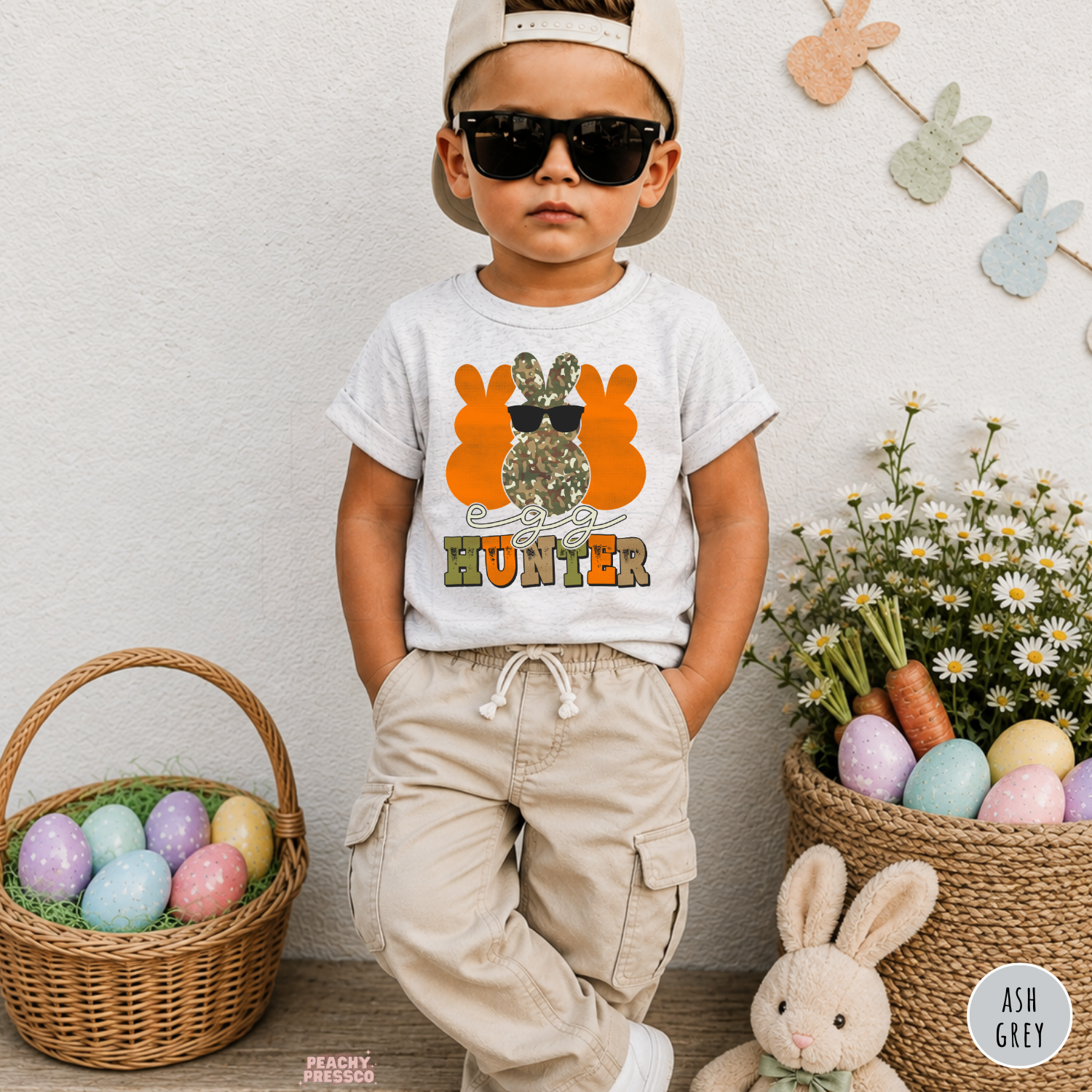 Toddler boy wearing an ash grey Egg Hunter Easter shirt with a camo bunny wearing sunglasses and rustic Easter graphic.