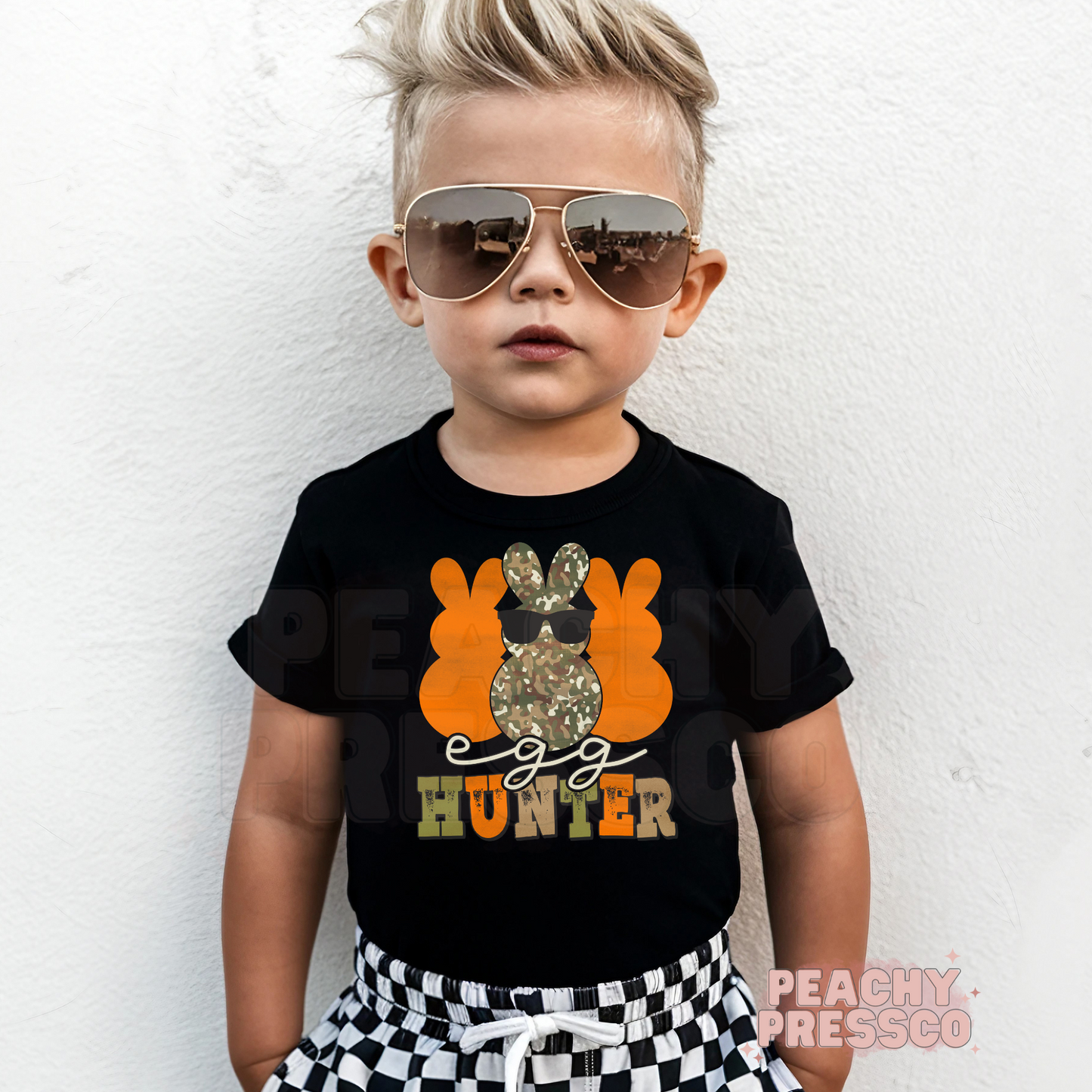 Toddler boy wearing a black Egg Hunter Easter tee with a camouflage bunny graphic and cool sunglasses design.