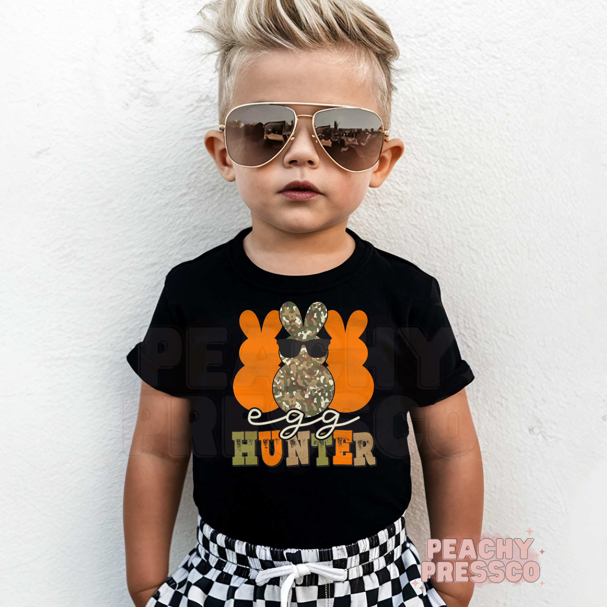 Toddler boy wearing a black Egg Hunter Easter tee with a camouflage bunny graphic and cool sunglasses design.