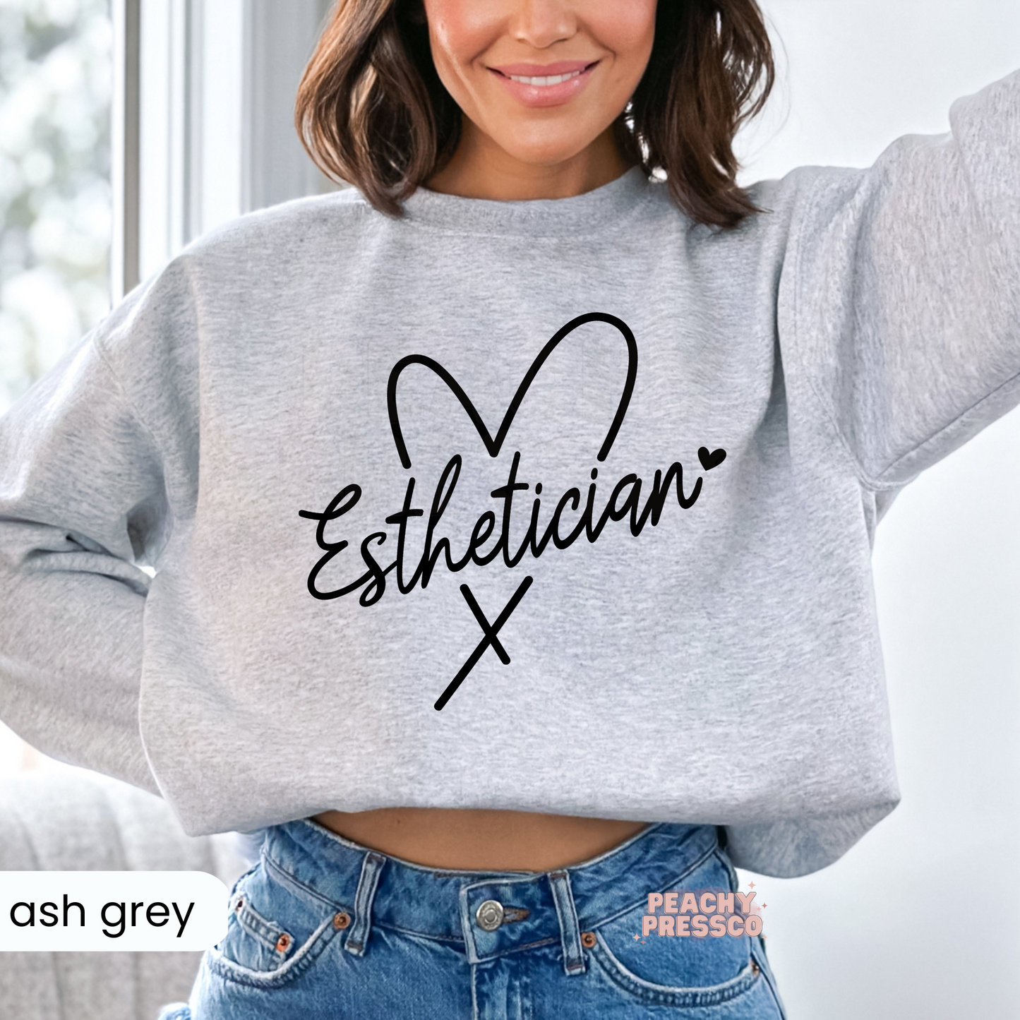 Ash grey crewneck sweatshirt featuring a minimalist Esthetician script design with a heart outline, perfect for estheticians, skincare professionals, and spa employees.