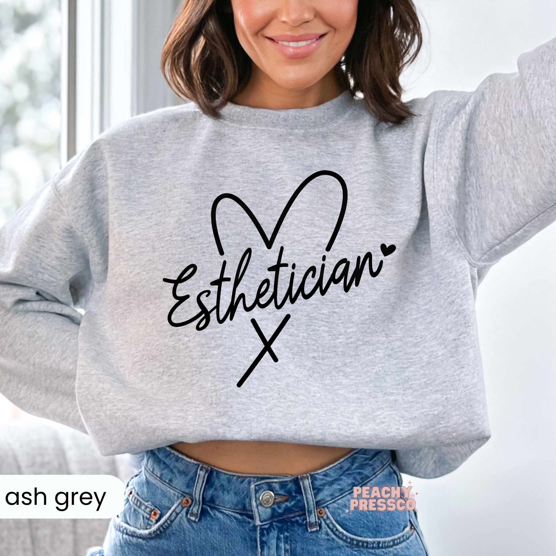 Ash grey crewneck sweatshirt featuring a minimalist Esthetician script design with a heart outline, perfect for estheticians, skincare professionals, and spa employees.