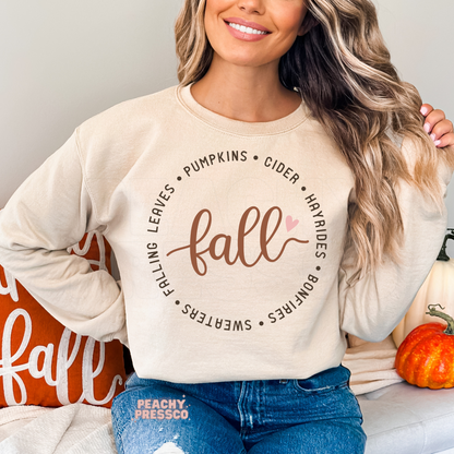 Woman wearing a sand crewneck sweatshirt featuring a simple autumn typography design with pumpkins, cider, hayrides, bonfires, sweaters, and falling leaves.