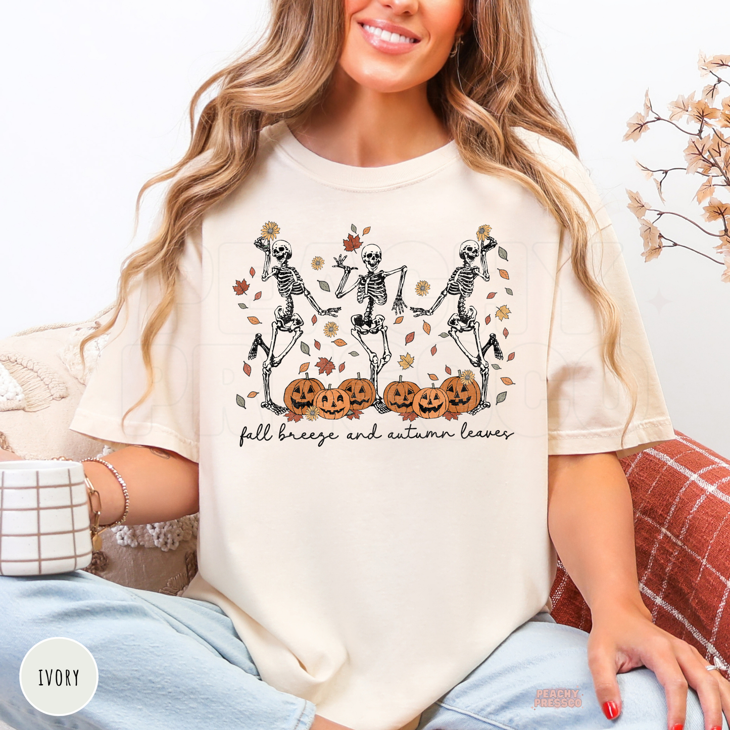 Woman wearing an ivory Comfort Colors t-shirt with dancing skeletons, pumpkins, autumn leaves, and "Fall Breeze and Autumn Leaves" graphic.