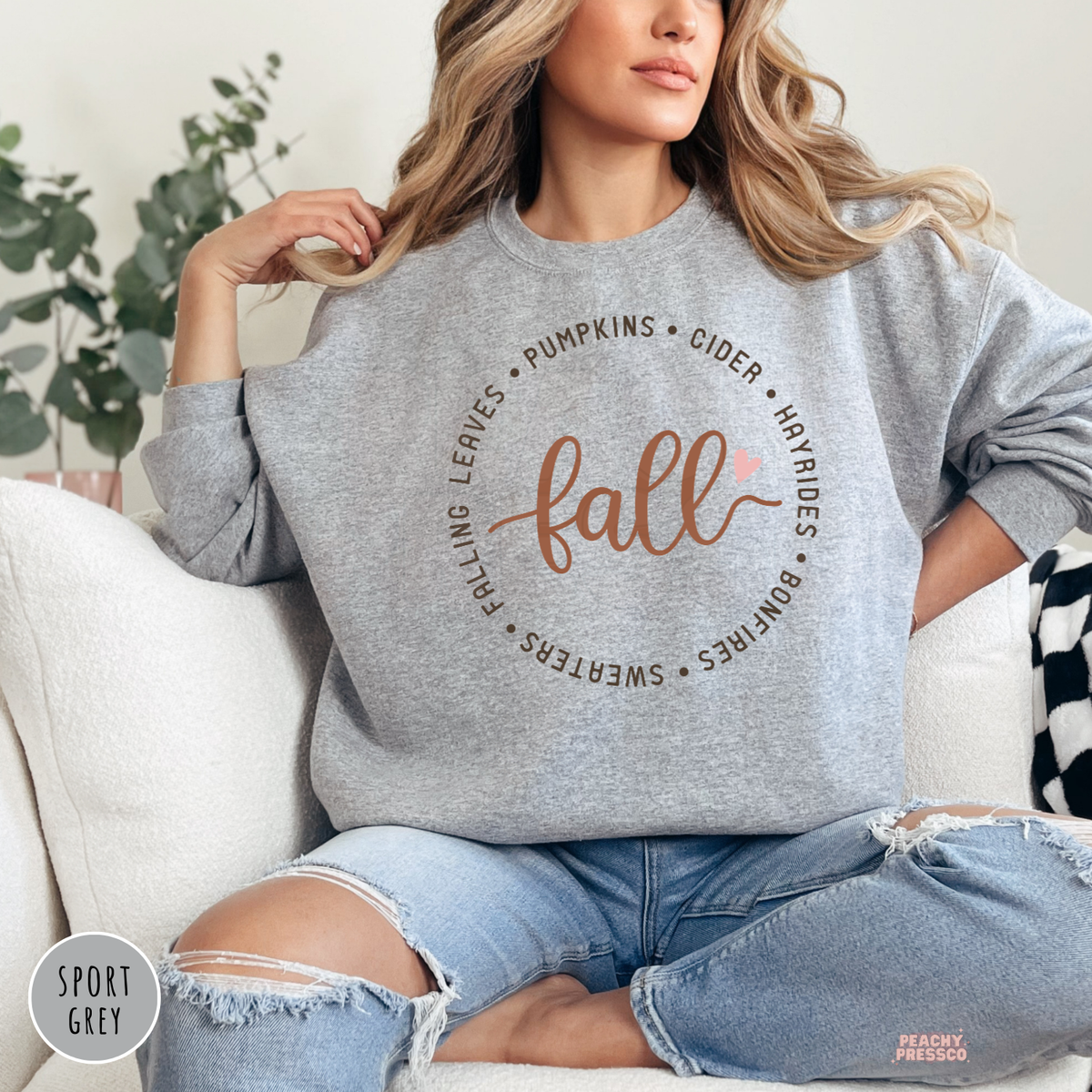 Woman wearing a sport grey sweatshirt featuring a minimalist fall typography design with leaves, pumpkins, cider, hayrides, bonfires, and sweaters.