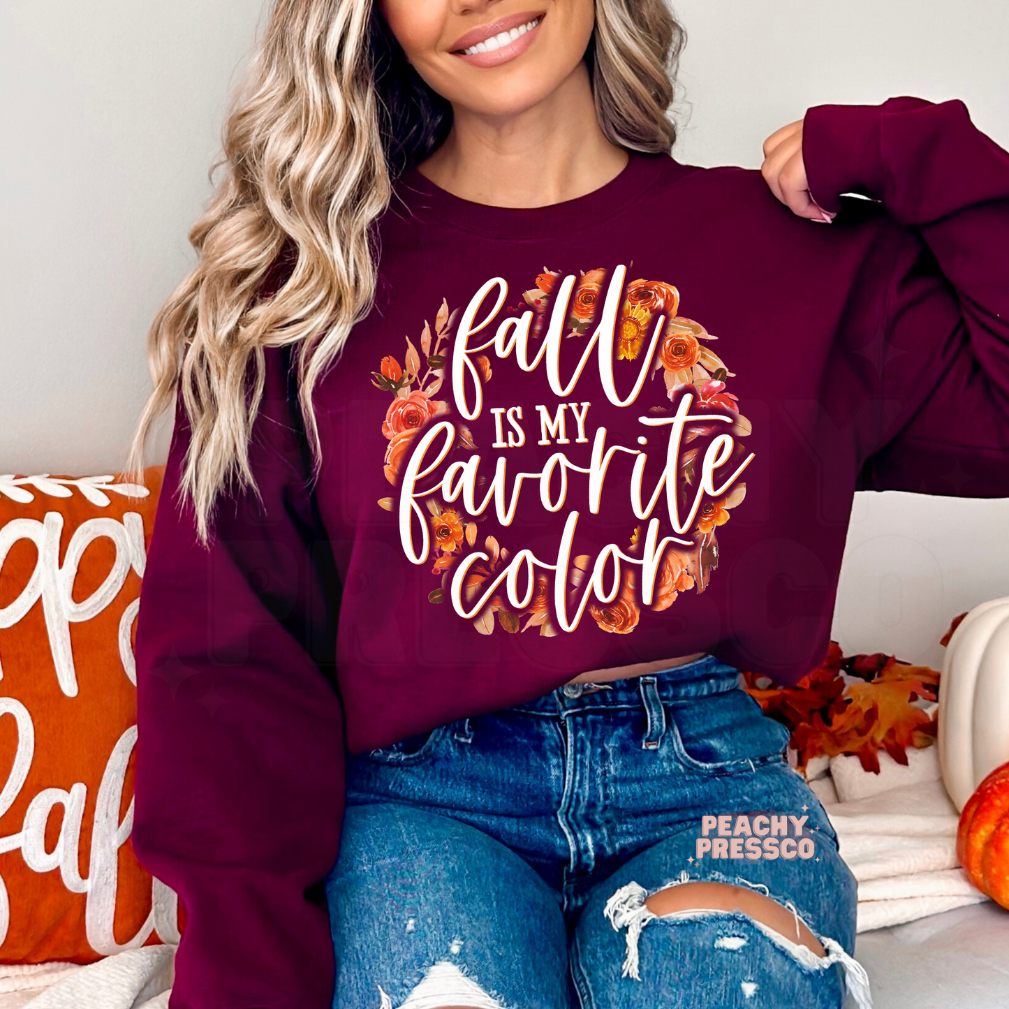 Woman wearing a maroon crewneck sweatshirt featuring a floral "Fall Is My Favorite Color" autumn design with warm fall flowers.