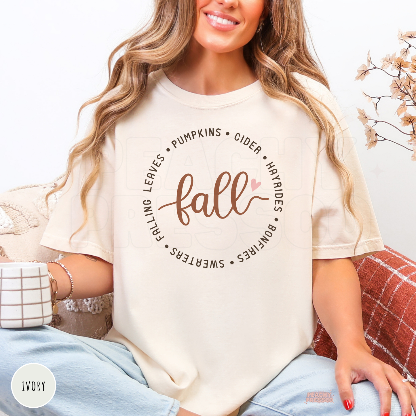Woman wearing an ivory Comfort Colors t-shirt featuring a stylish fall script design with pumpkins, cider, hayrides, bonfires, sweaters, and falling leaves.