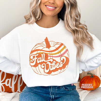 Woman wearing a white crewneck sweatshirt with a retro Fall Vibes pumpkin graphic in warm vintage fall colors.