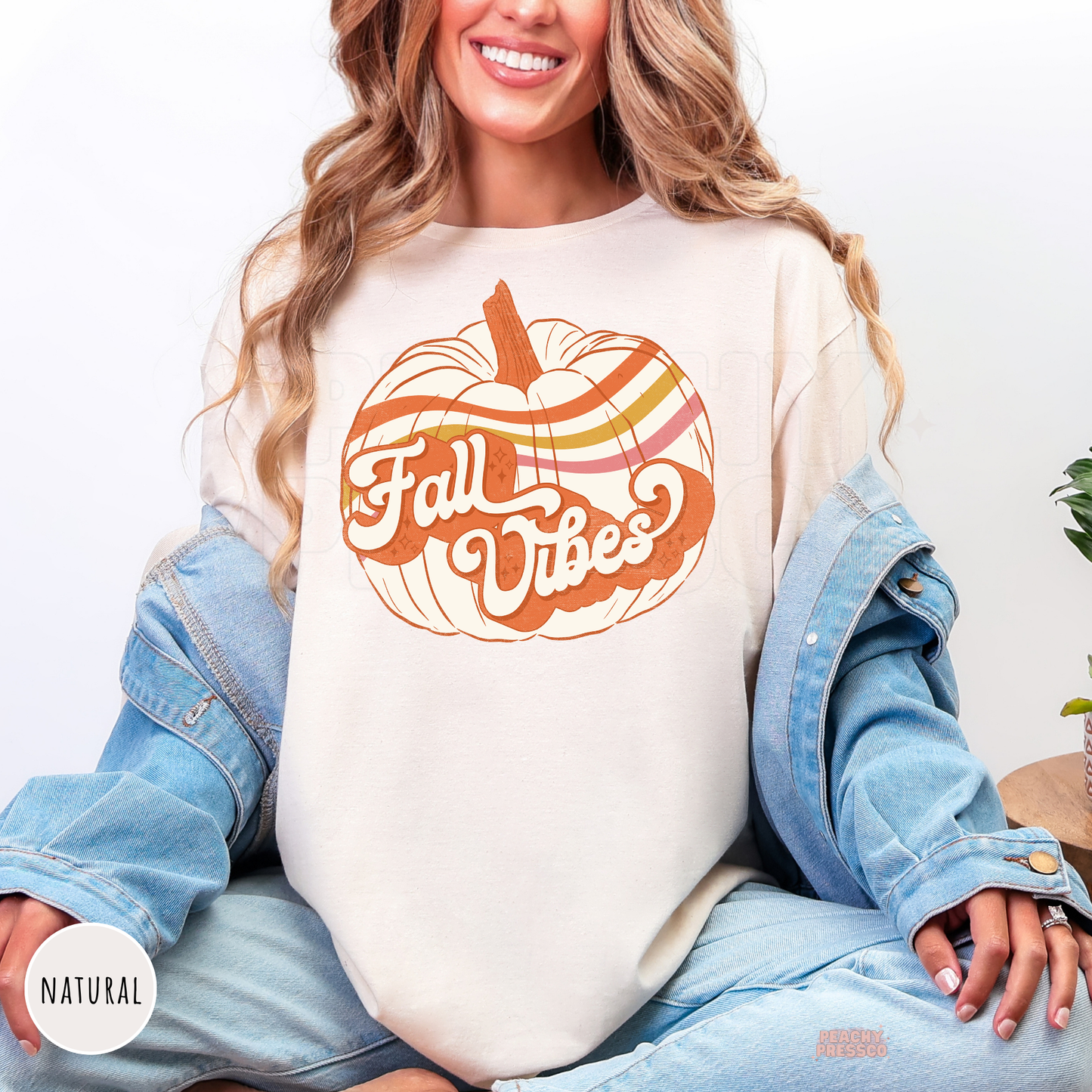Woman wearing a natural graphic t-shirt featuring a vintage Fall Vibes pumpkin design in warm retro autumn colors.