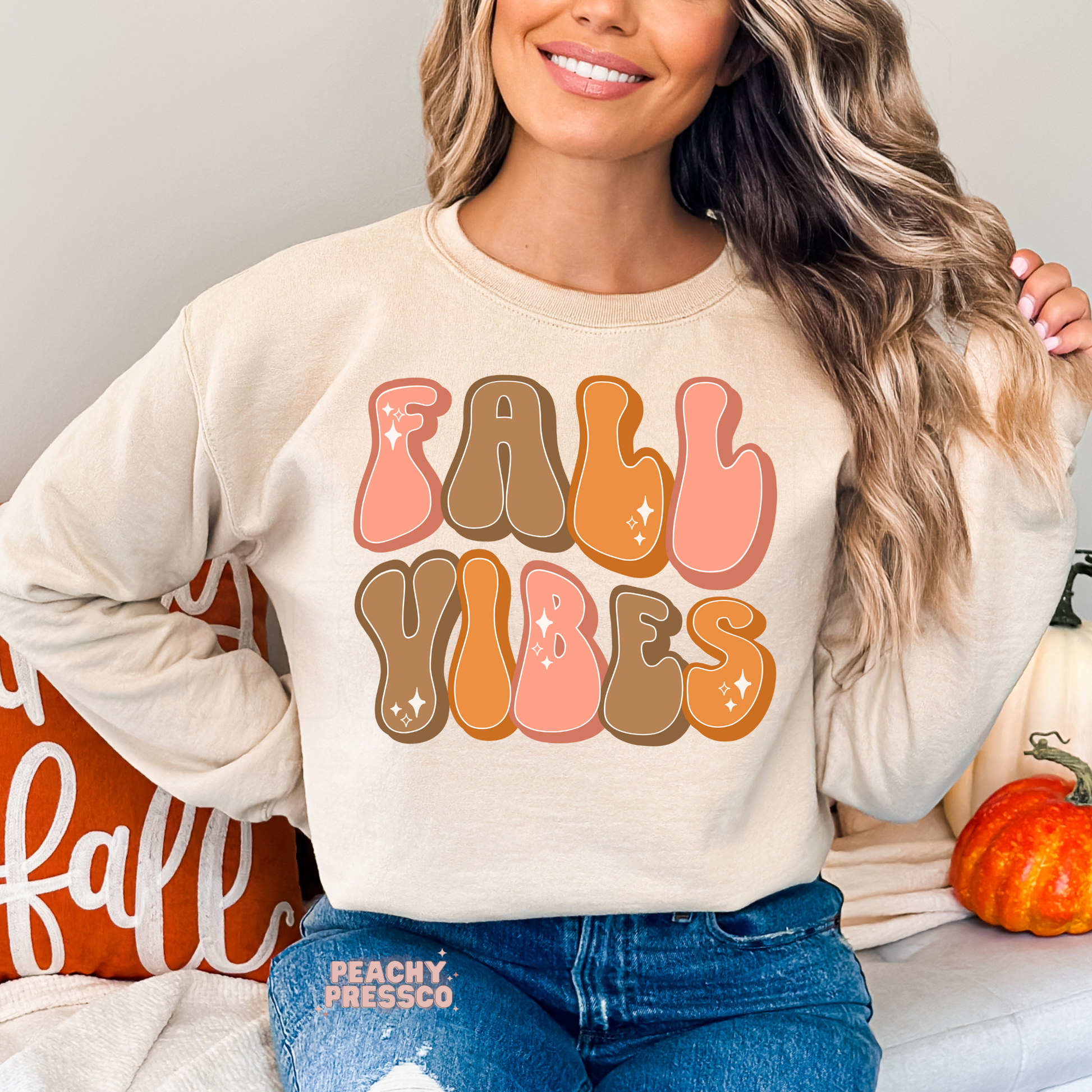 Woman wearing a sand crewneck sweatshirt with a colorful retro "Fall Vibes" typography design in warm autumn tones.