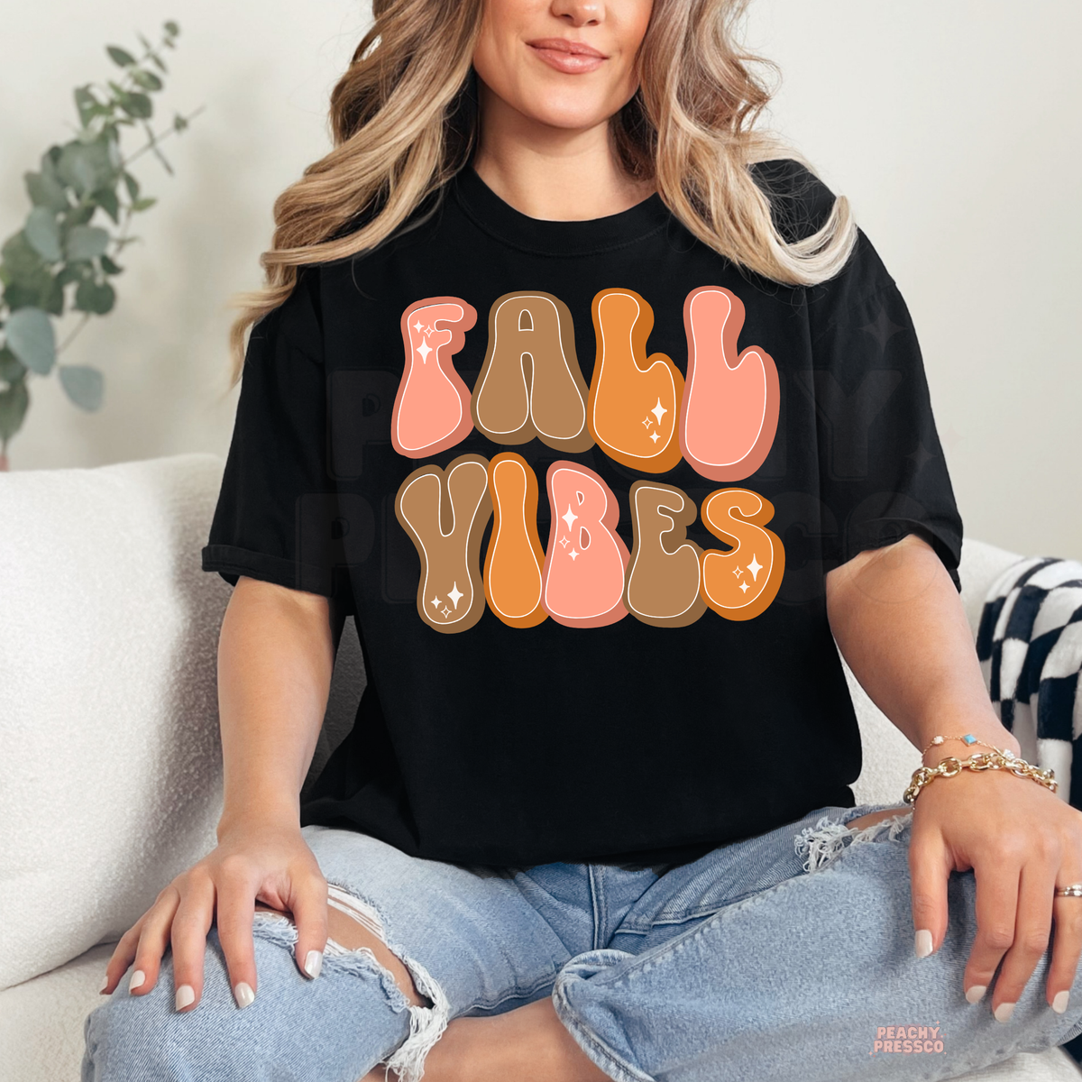 Woman wearing a black t-shirt featuring a colorful retro "Fall Vibes" graphic with pink, orange, and brown bubble letters.