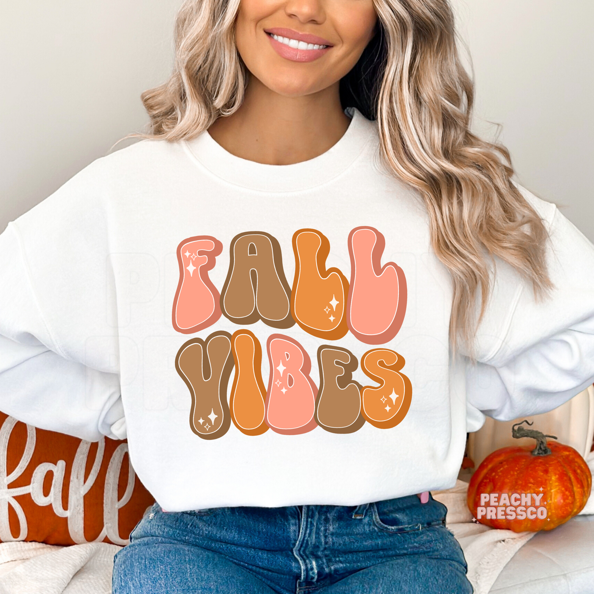 Woman wearing a white crewneck sweatshirt featuring a trendy retro "Fall Vibes" graphic with pink, orange, and brown bubble letters.