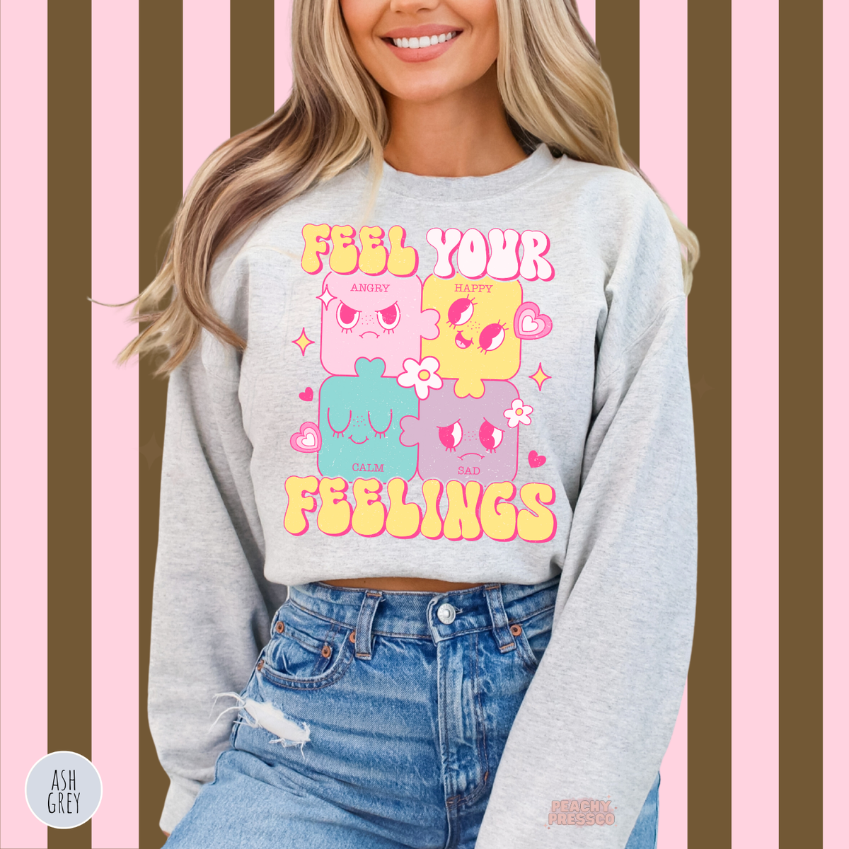 Ash grey Feel Your Feelings sweatshirt featuring adorable pastel puzzle faces representing different emotions with bright pink outlines and retro lettering.