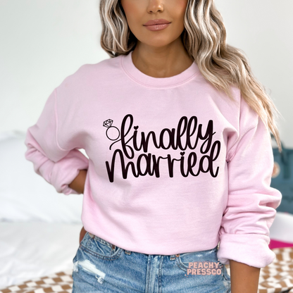 Light pink crewneck sweatshirt featuring the "Finally Married" graphic with a diamond ring illustration, perfect for newlyweds, honeymoon trips, post-wedding celebrations, bridal gifts, and wedding keepsakes.