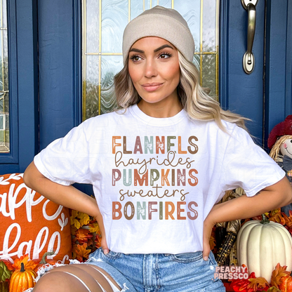 Woman wearing a white graphic t-shirt with a colorful "Flannels Hayrides Pumpkins Sweaters Bonfires" design for fall and autumn lovers.