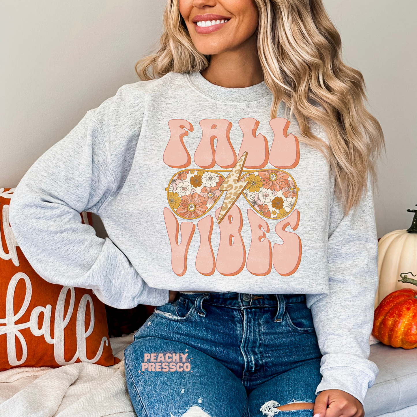 Woman wearing an ash grey crewneck sweatshirt featuring a retro Fall Vibes graphic with floral sunglasses, leopard lightning bolt, and vintage lettering.