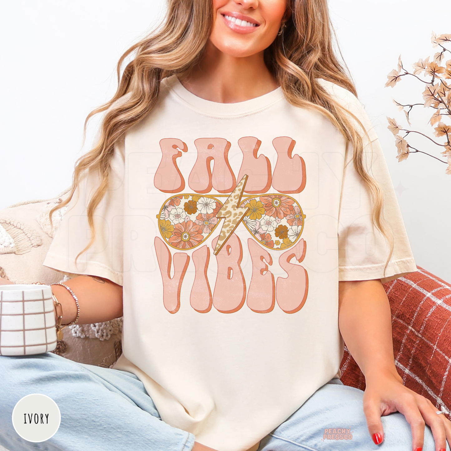 Woman wearing an ivory graphic t-shirt featuring a retro Fall Vibes design with floral sunglasses and a leopard lightning bolt.