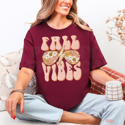 Woman wearing a maroon graphic t-shirt featuring a retro Fall Vibes design with floral sunglasses and a leopard print lightning bolt.