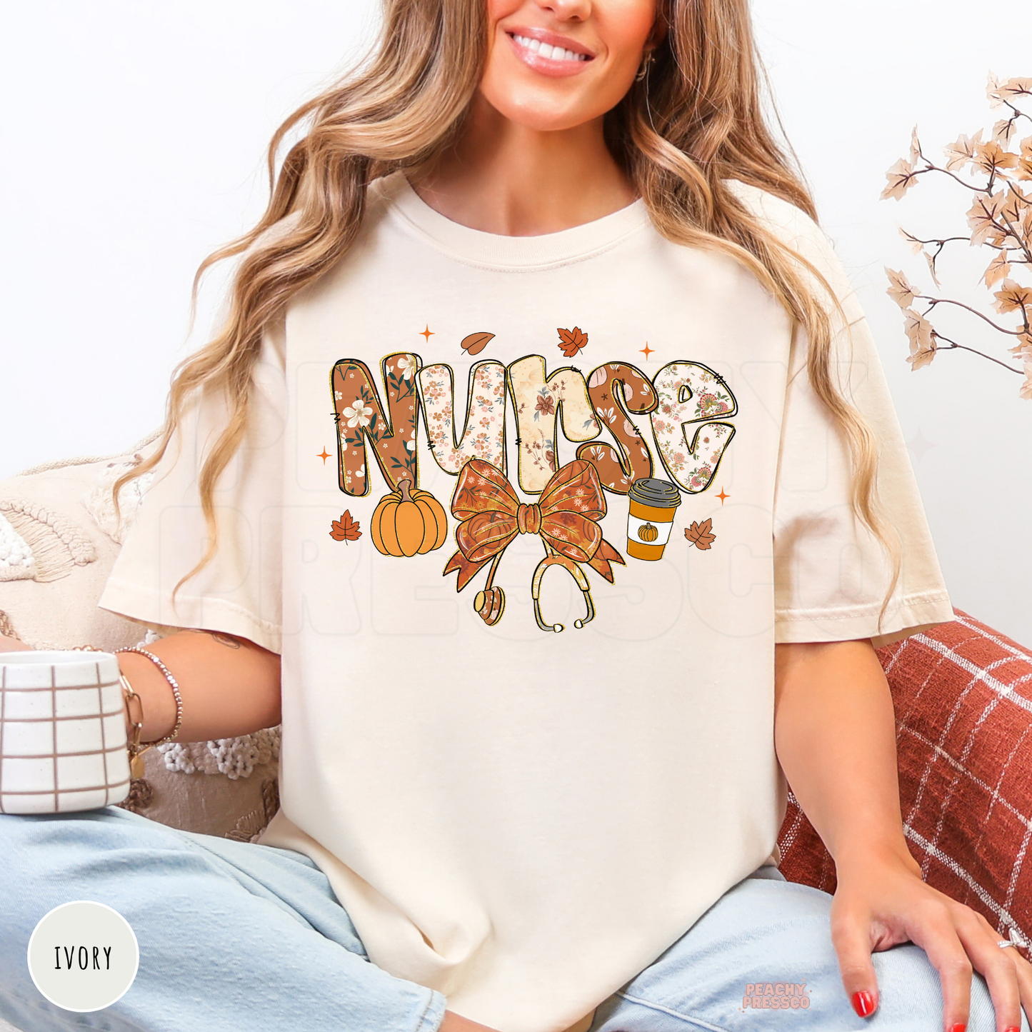 Woman wearing an ivory graphic t-shirt with a floral "Nurse" design featuring a pumpkin, pumpkin spice coffee, stethoscope bow, and fall leaves.