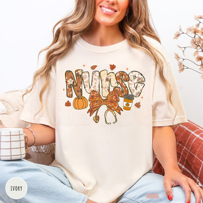 Woman wearing an ivory graphic t-shirt with a floral "Nurse" design featuring a pumpkin, pumpkin spice coffee, stethoscope bow, and fall leaves.