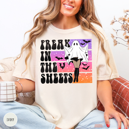Woman wearing an ivory Comfort Colors Halloween t-shirt featuring a funny "Freak in the Sheets" ghost graphic with fishnet stockings, bats and retro sunset.