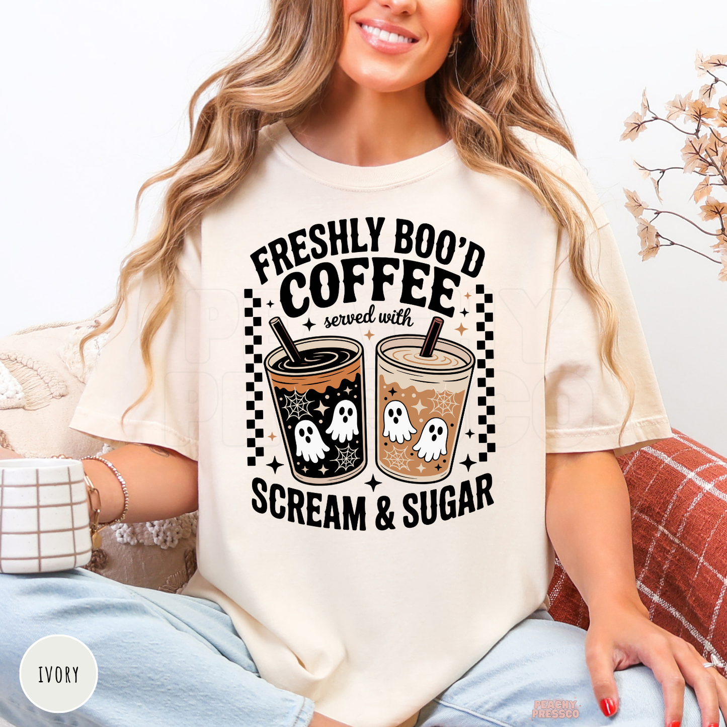 Woman wearing an ivory Halloween t-shirt featuring a Freshly Boo'd Coffee Served with Scream & Sugar design with spooky ghost iced coffees and fall coffee aesthetic.