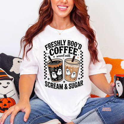 Woman wearing a white Halloween t-shirt featuring the Freshly Boo'd Coffee Served with Scream & Sugar ghost coffee graphic with spooky iced coffees.
