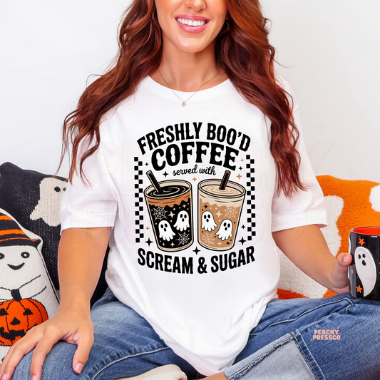 Woman wearing a white Halloween t-shirt featuring the Freshly Boo'd Coffee Served with Scream & Sugar ghost coffee graphic with spooky iced coffees.