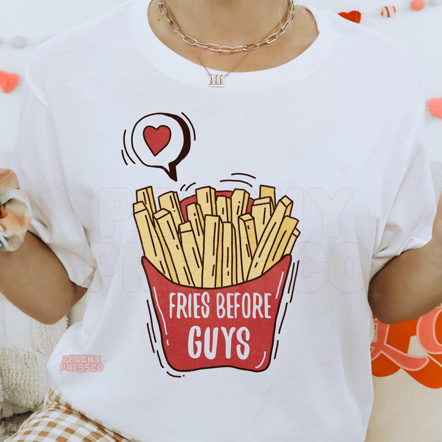Close-up of a white graphic t-shirt featuring a vintage-style "Fries Before Guys" french fry design with a heart accent.