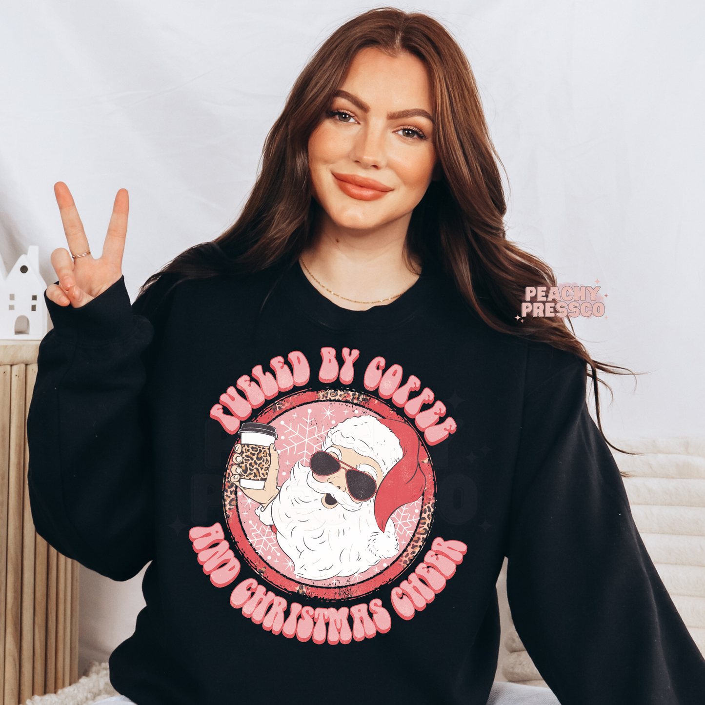 Women throwing a peace sign wearing a black sweatshirt with a retro cool Santa holding a leopard print coffee cup that reads Fueled By Coffee And Christmas Cheer.