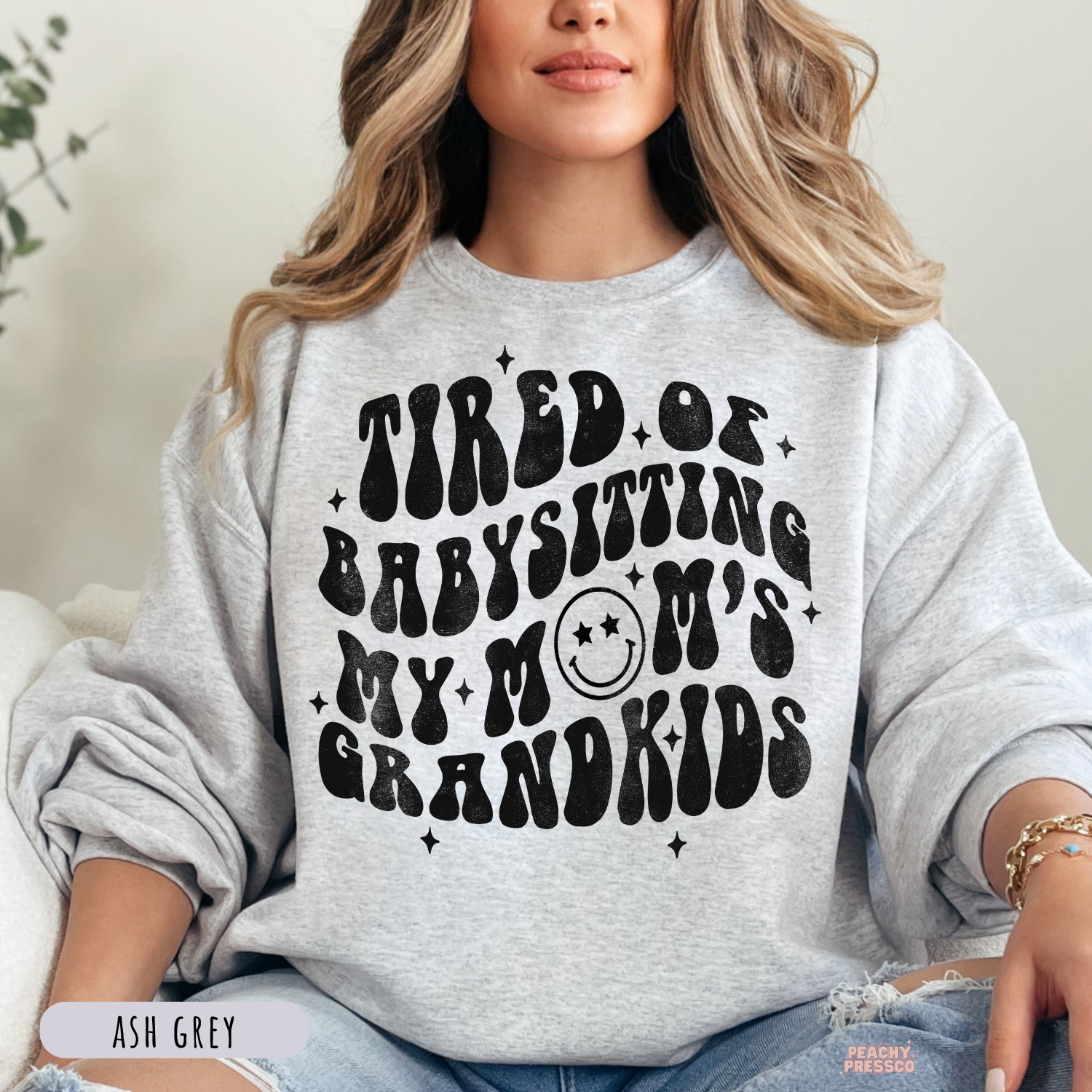 Ash Grey sweatshirt featuring the playful "Tired of Babysitting My Mom's Grandkids" retro graphic. Funny motherhood sweatshirt with a vintage aesthetic.