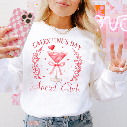 White sweatshirt showcasing a Galentine's Day Social Club graphic with a pink cocktail, heart garnish, floral laurels, and coquette-inspired Valentine's style.