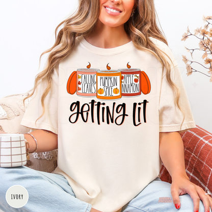 Woman wearing an ivory Comfort Colors t-shirt with a funny "Getting Lit" fall candle design inspired by pumpkin spice and cozy autumn vibes.