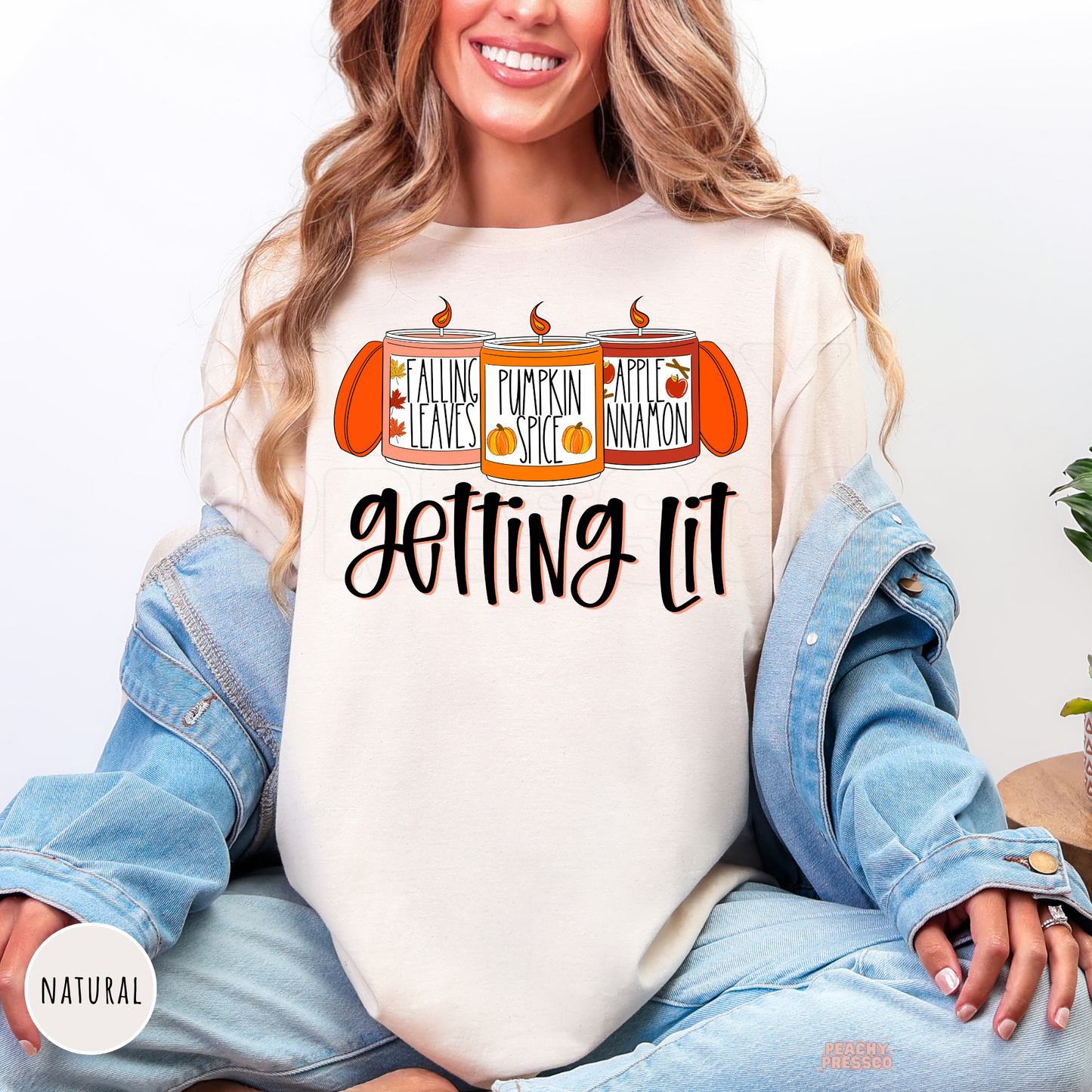 Woman wearing a natural graphic t-shirt featuring a funny "Getting Lit" fall candle design with pumpkin spice, falling leaves, and apple cinnamon artwork.